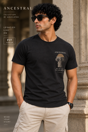 A man wearing a black crew-neck t-shirt with a beige graphic print of an ancient column and the word 'ANCESTRAL', paired with beige cargo shorts, standing in front of a stone column.